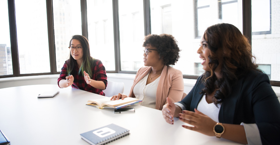 Three women talking at a conference table. 