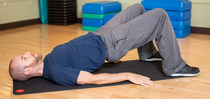 Young man laying on floor showing bridge hip raise end movement