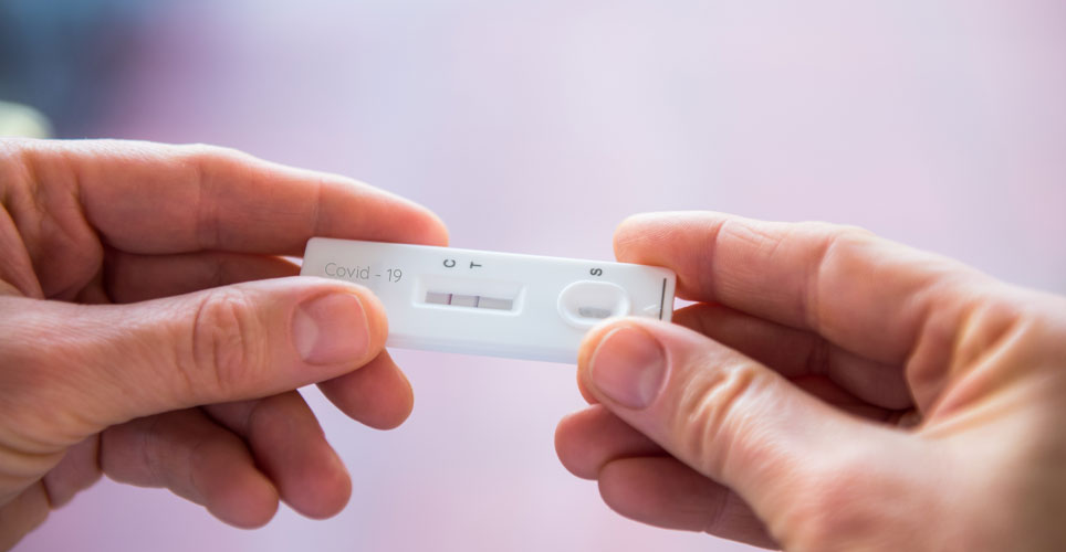 Close up of two White hands holding a white, rectangular COVID-19 test