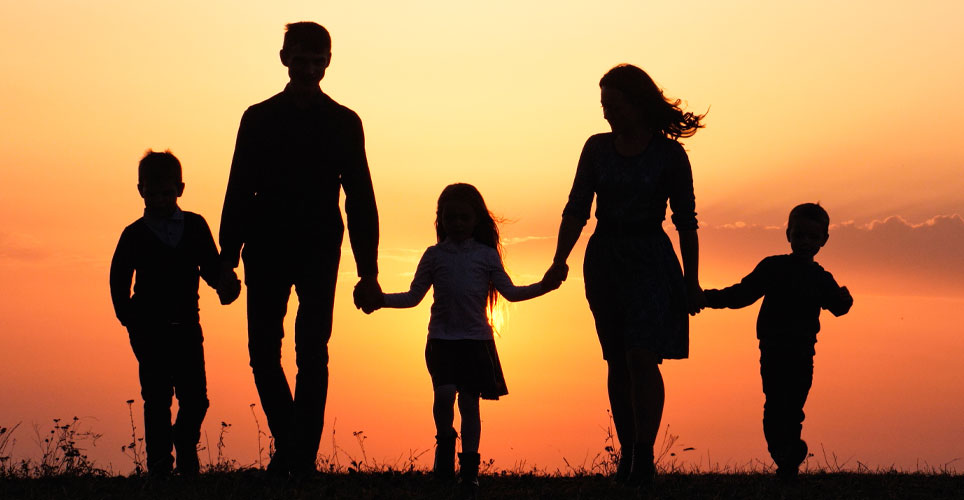 Backlit shot of a family of five with two parents and three small children walking toward the camera, hand in hand