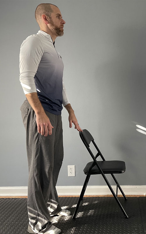 man standing with hand on the back of a chair