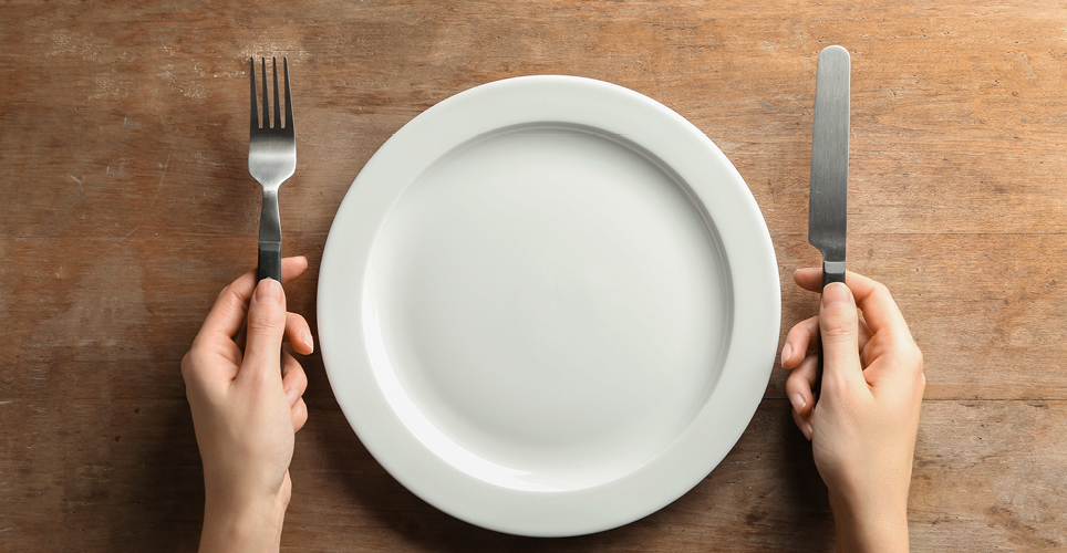 A person with a fork and knife, sitting in front of an empty plate
