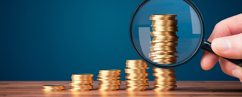 a hand holding a magnifying glass up to a stacks of coins