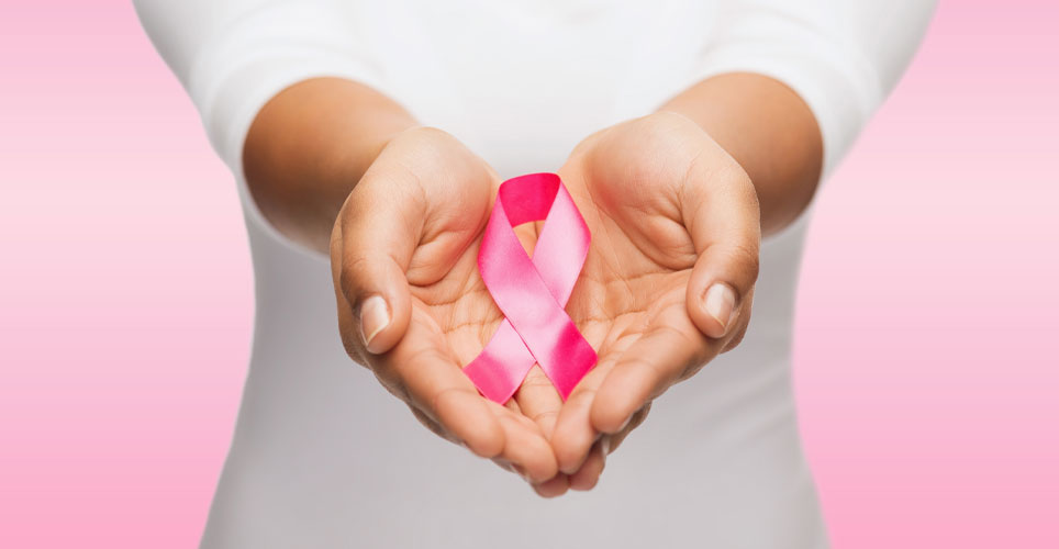 Close up of a woman's torso with her two hands cupping a pink ribbon