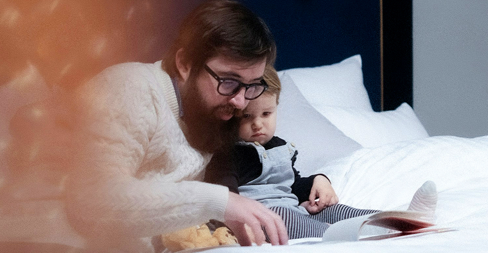 Adult man reading to a toddler in bed