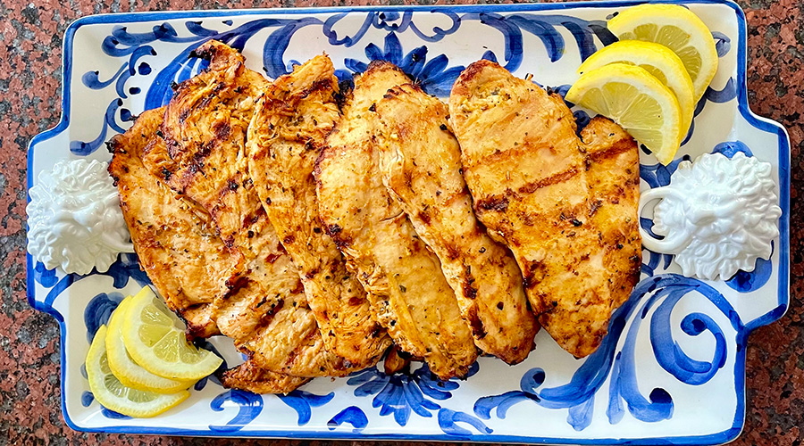 Greek chicken paillards plated with lemon on a hand painted dish.