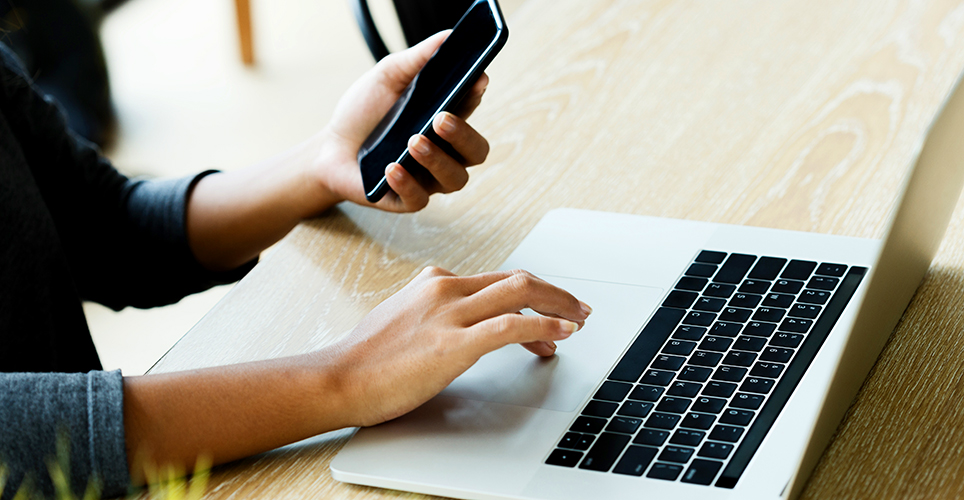 Close up of a woman's hands, one on a laptop and the other holding a cell phone