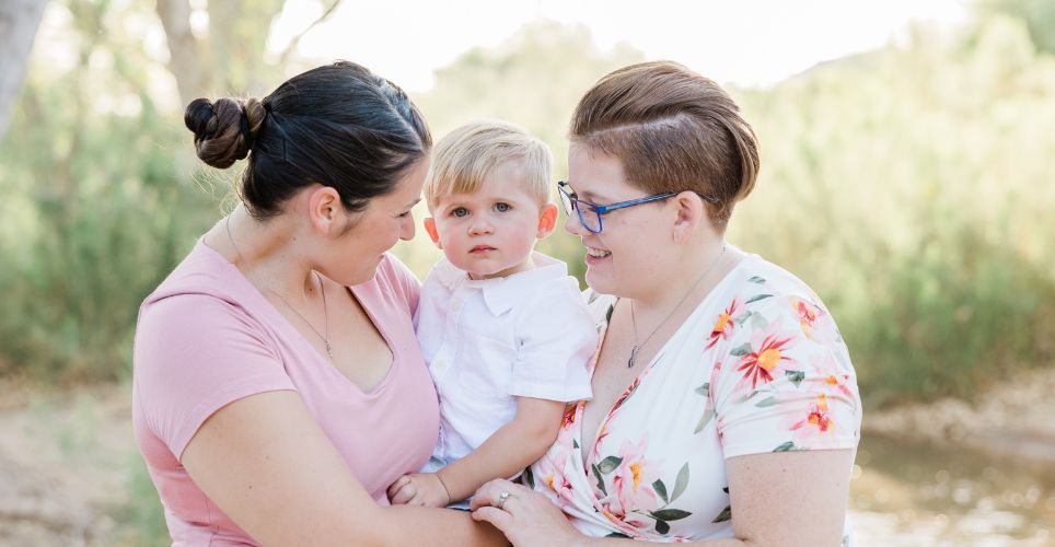 Two women smiling while holding a small child between them.