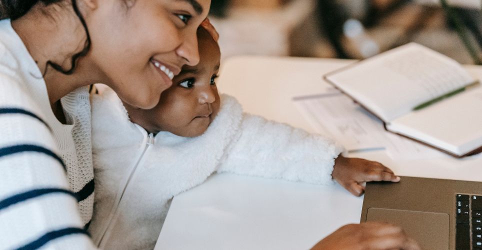 Woman holding baby while working on a laptop.