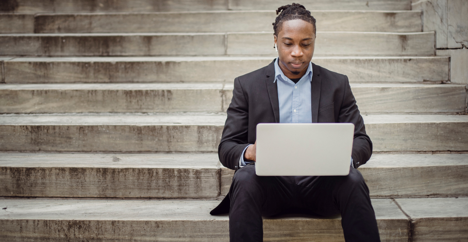 man sitting on steps outside with a laptop on his lap