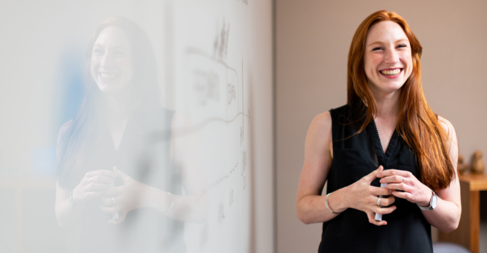 Woman standing in front of a white board with a smiling face.