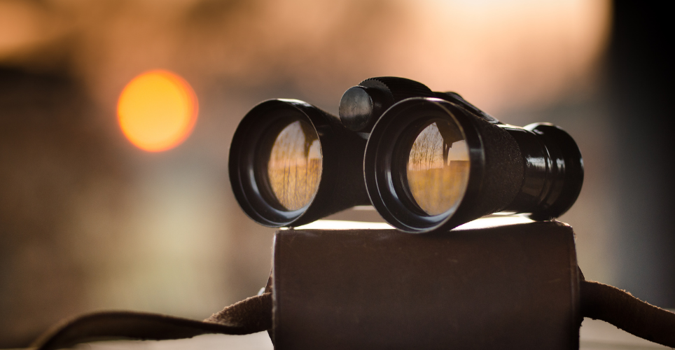 a pair of binoculars sitting on top of the case with the sun in the background