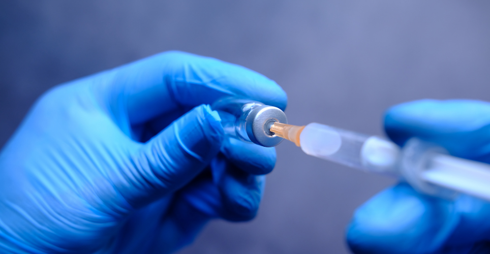 Person with gloves filling vaccine syringe.