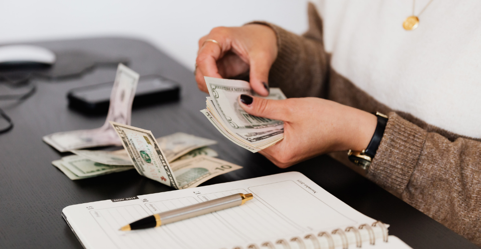 Close up of woman's hands holding green money bills with more bills scattered on a table before her