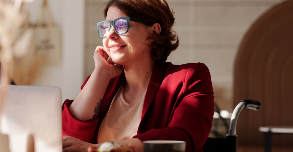 A woman dressed business casually, smiling and looking out above her laptop