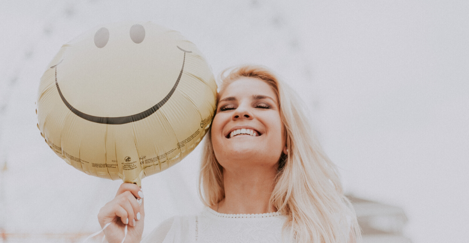 Woman with light hair smiling with relief, holding a smiley face balloon