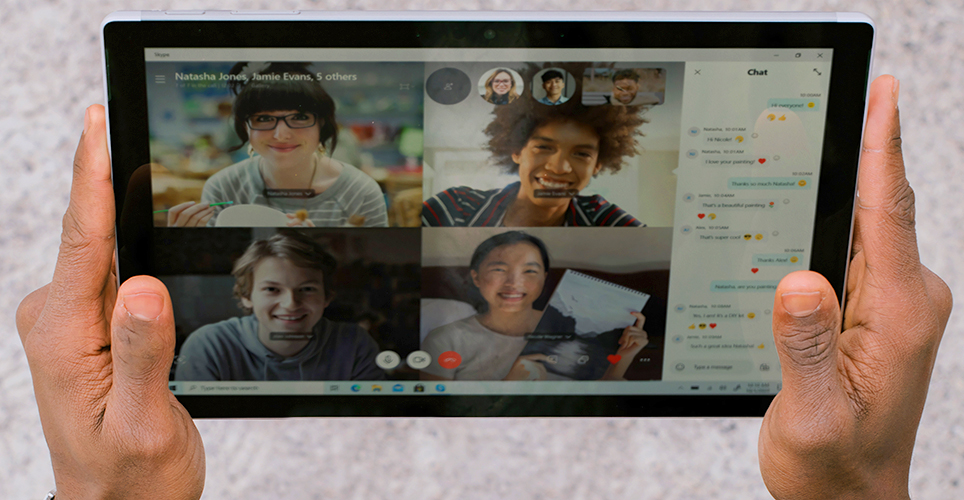 Hands holding a tablet with a video conference displayed that has four participants.