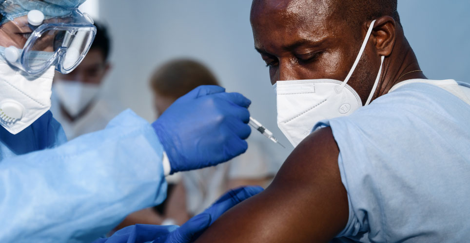 closeup of a medical person in full PPE giving an injection to a patient in a mask