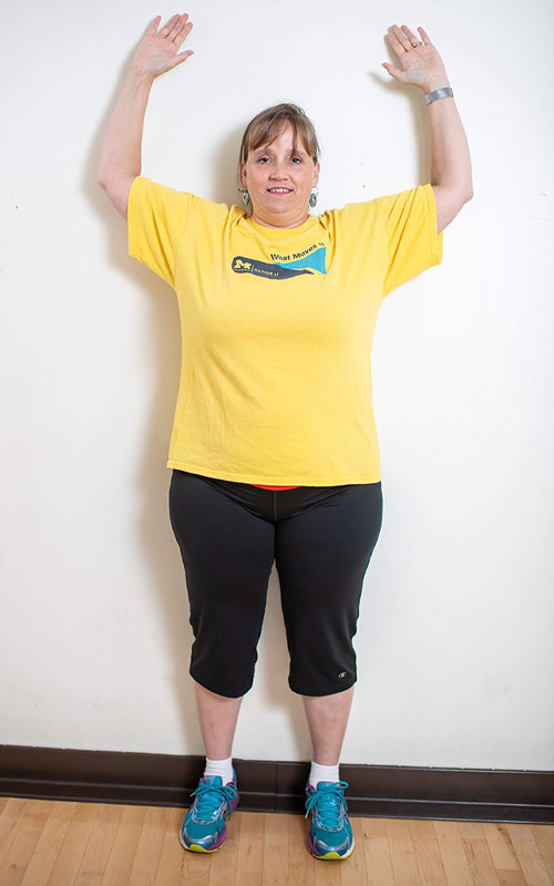 woman standing against wall with arms raised showing wall angels end movement