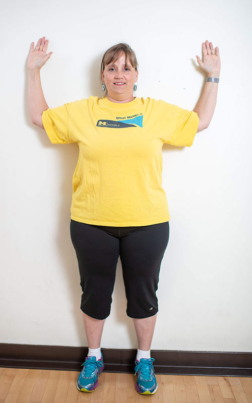 woman standing against wall with arms raised showing wall angels start movement